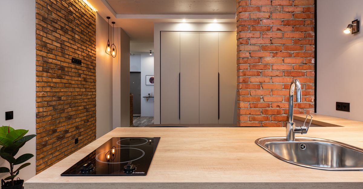 Piano cottura a induzione in vetroceramica nero incassato in un piano di lavoro in legno chiaro, in una cucina moderna con pareti in mattoni a vista.