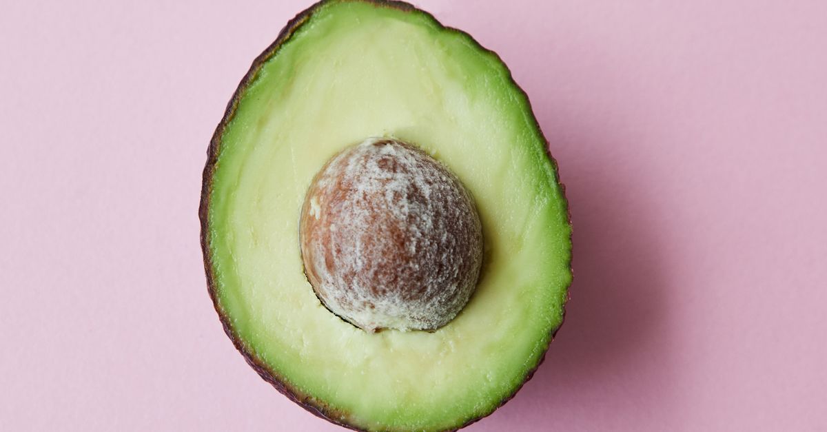 Metà di avocado con il nocciolo, appena tagliata e ancora di colore verde brillante, su sfondo rosa.