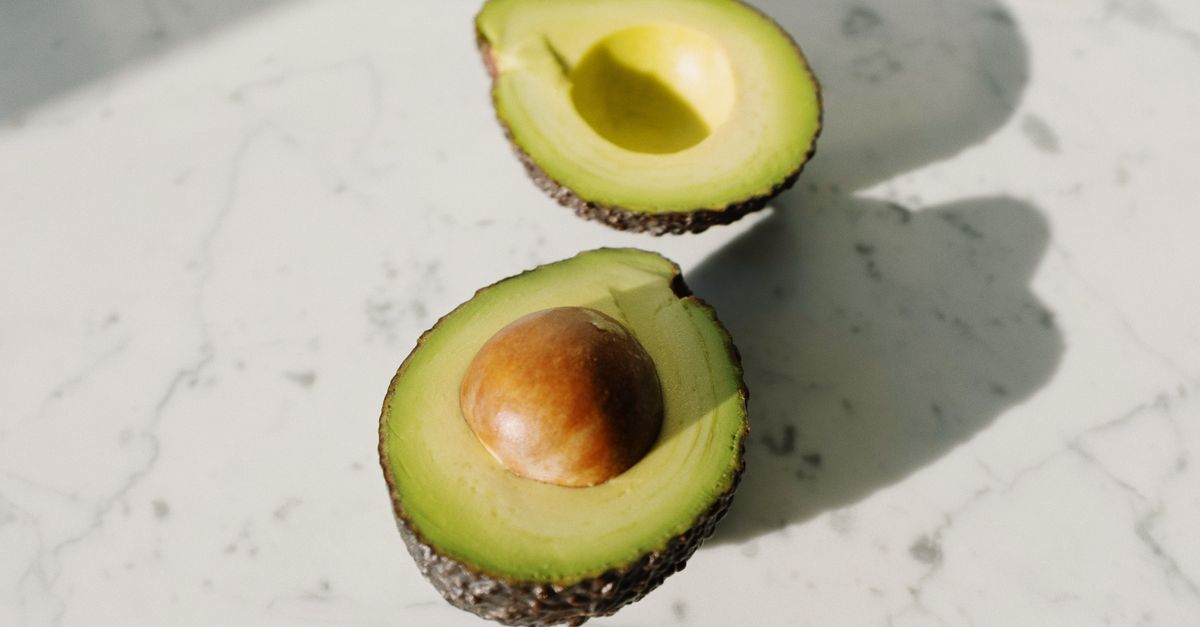 Un avocado tagliato a metà con il nocciolo, appoggiato su un piano in marmo bianco.