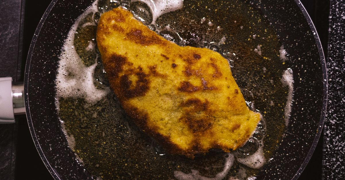 Una cotoletta impanata dorata e croccante frigge in una padella con olio e burro schiumoso.