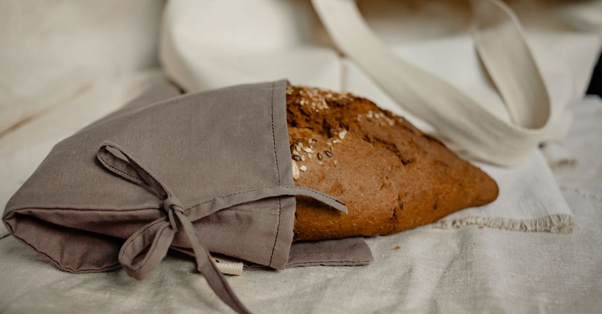 Un filone di pane rustico avvolto in un canovaccio di cotone grigio legato con un fiocco.