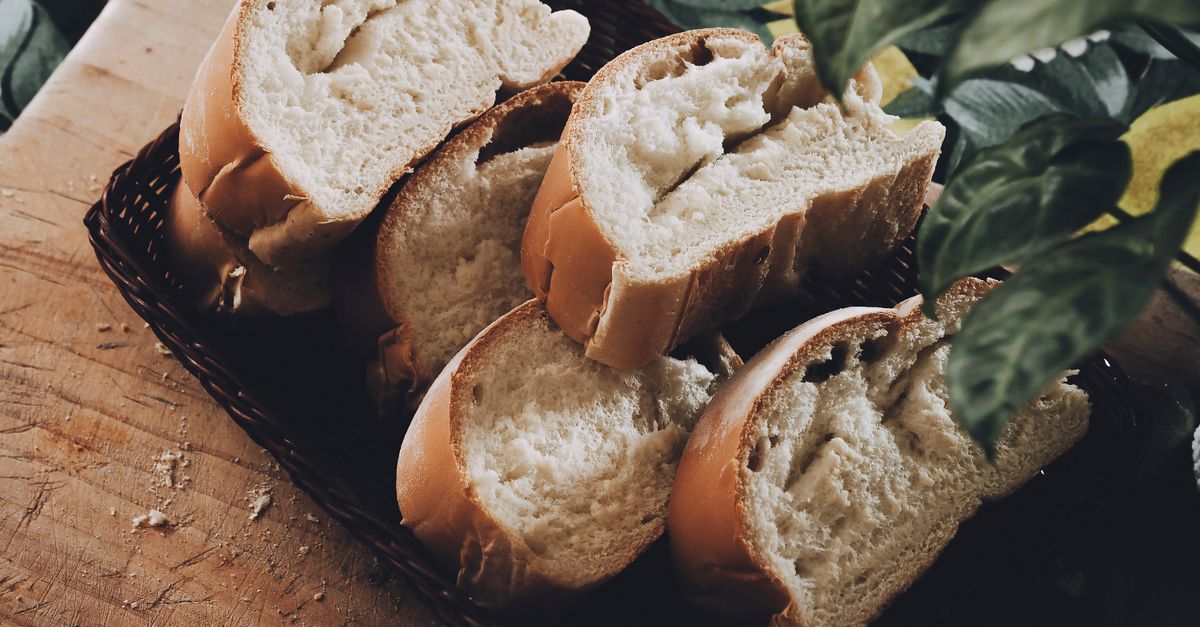 Fette di pane tagliate disposte in un cestino di vimini su un tagliere di legno.