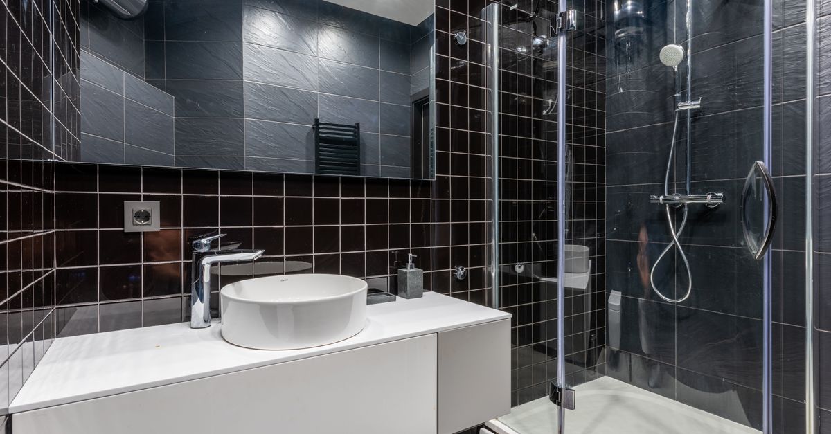 Bagno moderno con piastrelle scure, box doccia in vetro e lavabo bianco puliti e senza aloni di calcare.