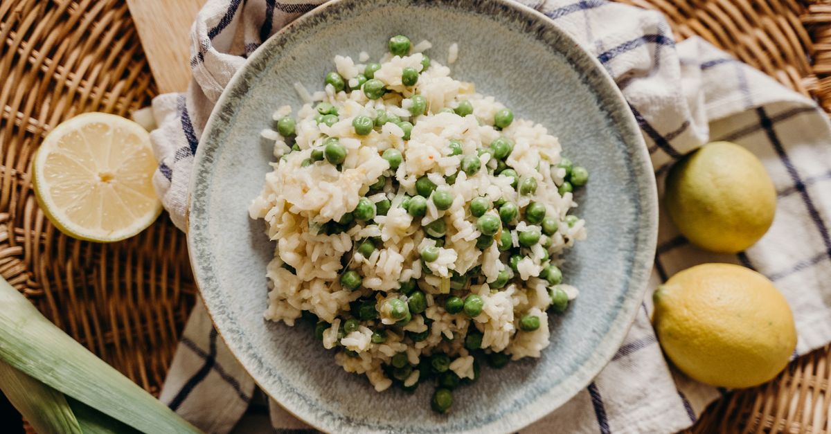 Un piatto in ceramica con risotto cremoso ai piselli, guarnito con verdure e servito su un vassoio di vimini con limoni accanto.
