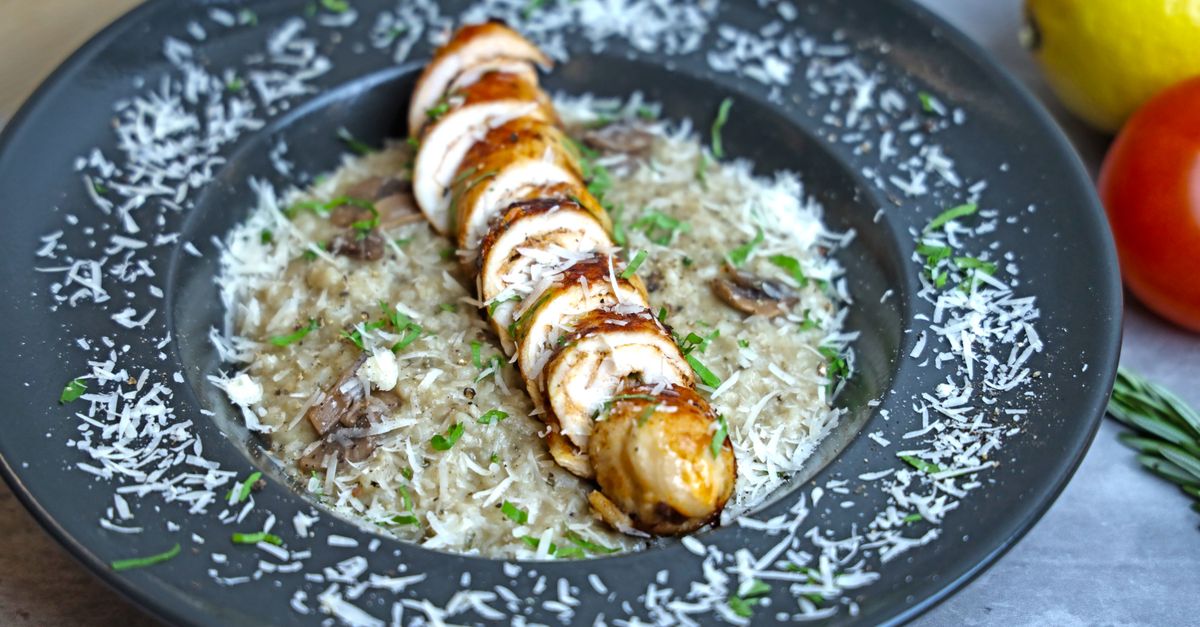 Risotto ai funghi guarnito con scaglie di parmigiano e glassa balsamica, servito su un piatto scuro con pomodoro e limone sullo sfondo.