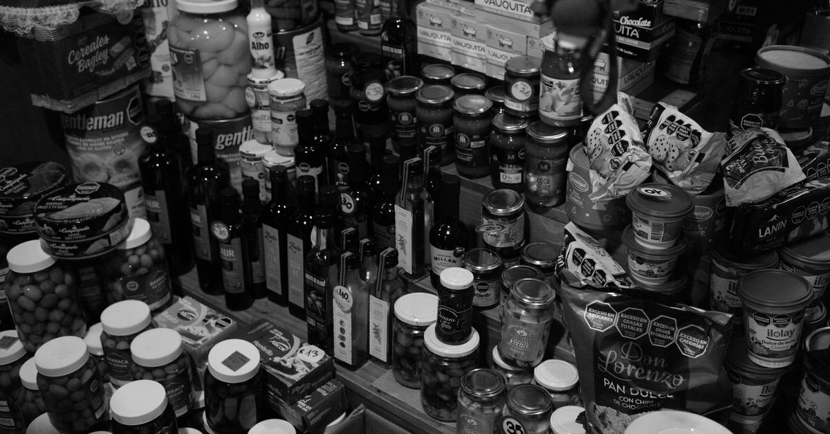 Scaffali di legno con bottiglie di olio, barattoli e conserve disposti in una dispensa in bianco e nero