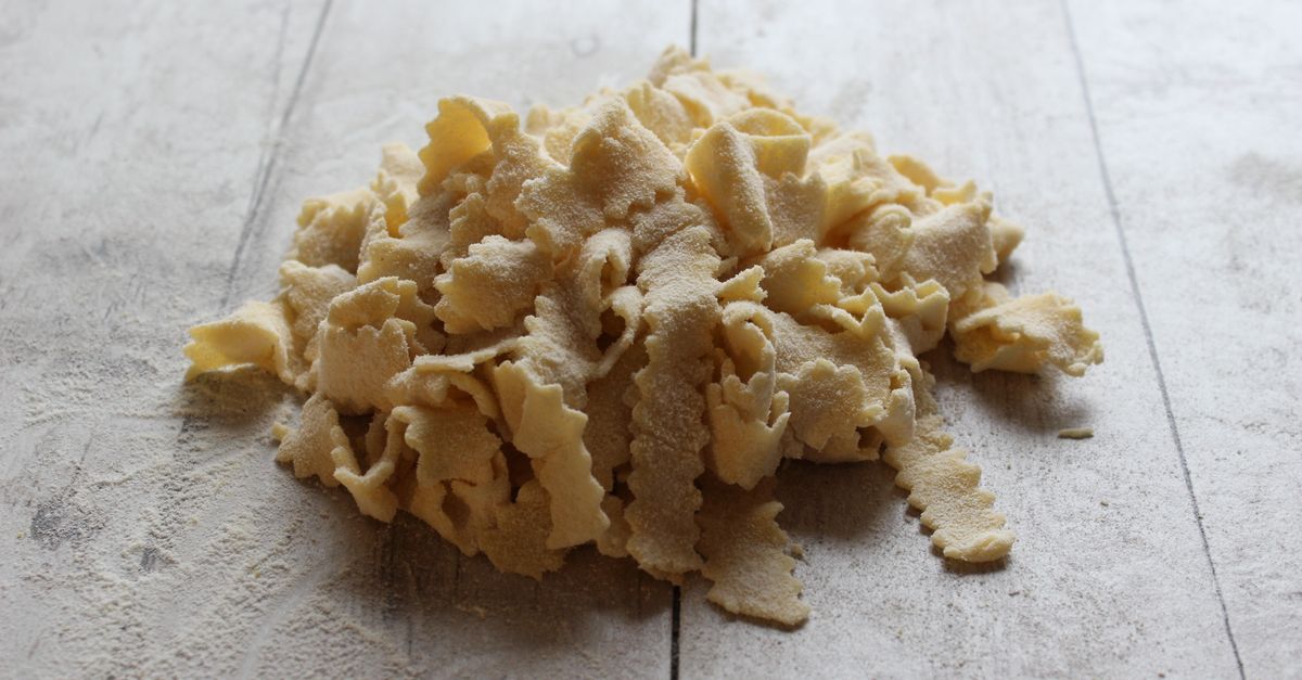 Pasta fresca fatta in casa, tagliata a pezzi irregolari e spolverata di farina, disposta su un tavolo di legno chiaro.