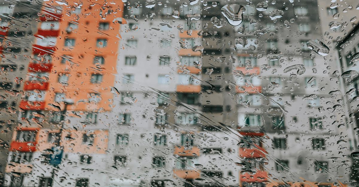 Vetro di una finestra coperto di gocce di pioggia con vista sfocata su palazzi colorati sullo sfondo, giornata piovosa