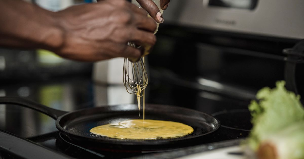 Una persona versa uovo sbattuto con una frusta in una padella calda sul fornello, iniziando a cuocere una frittata.