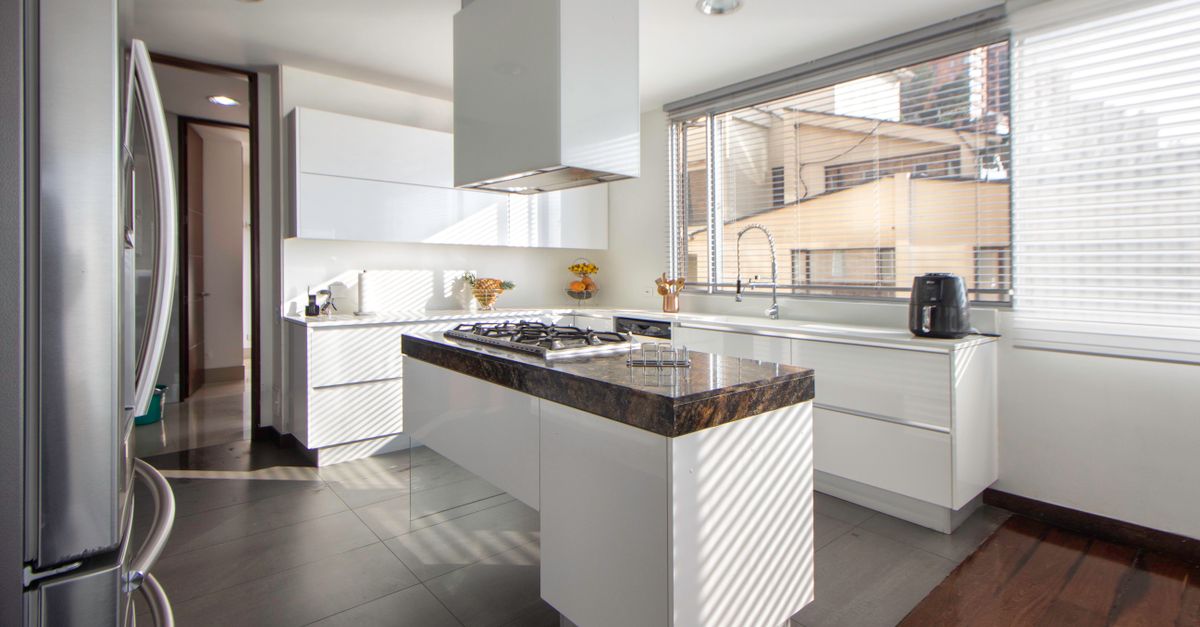 Cucina moderna bianca con isola centrale in marmo scuro e piano cottura in acciaio inox lucido incassato.