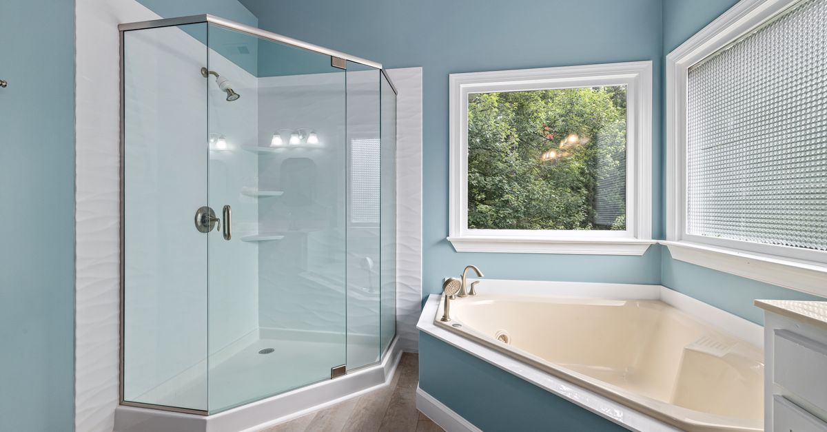 Box doccia in vetro con pareti azzurre e vasca da bagno in un moderno bagno luminoso.