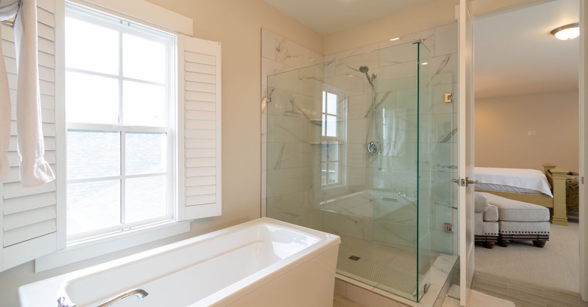 Bagno moderno con vasca, doccia in vetro e finestra con persiane bianche che lascia entrare luce naturale.