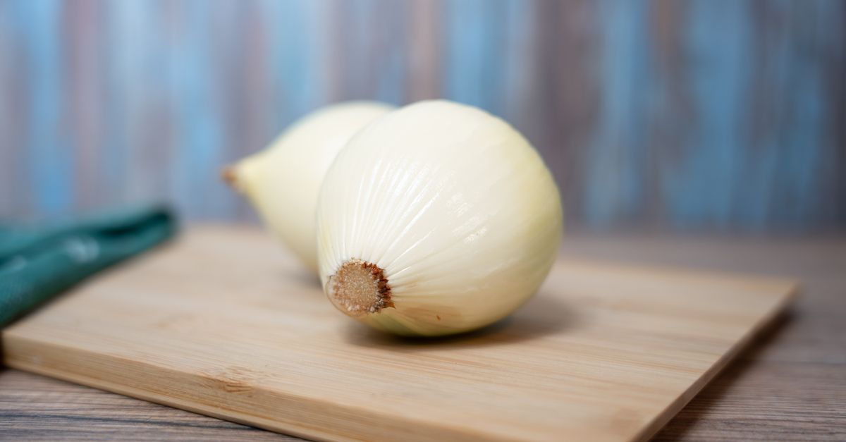 Due cipolle bianche intere appoggiate su un tagliere di legno.