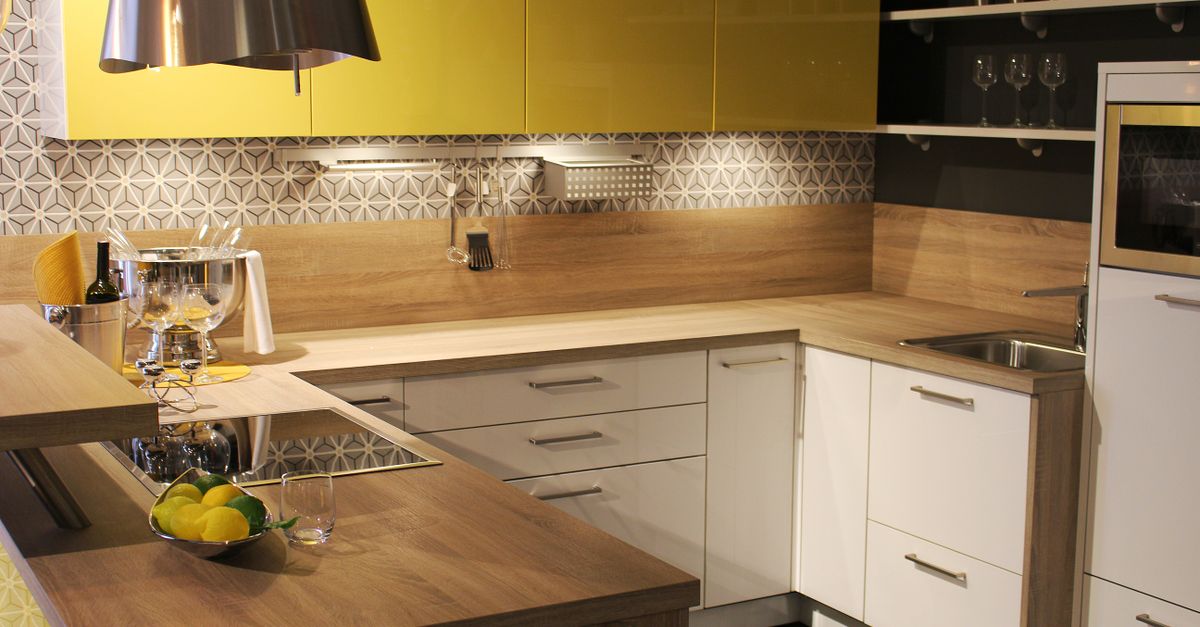 Cucina moderna con ante gialle e bianche, piano in legno e una ciotola di limoni gialli in primo piano.