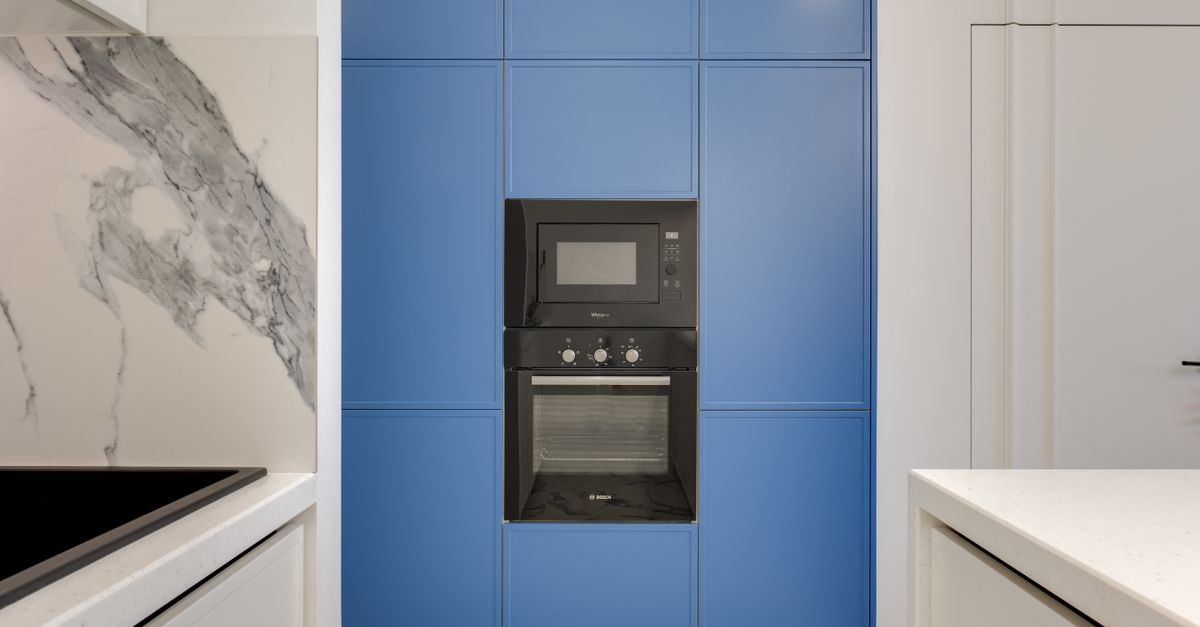 Forno da incasso nero integrato in una colonna di mobili blu, con microonde sopra e piano cucina bianco accanto.