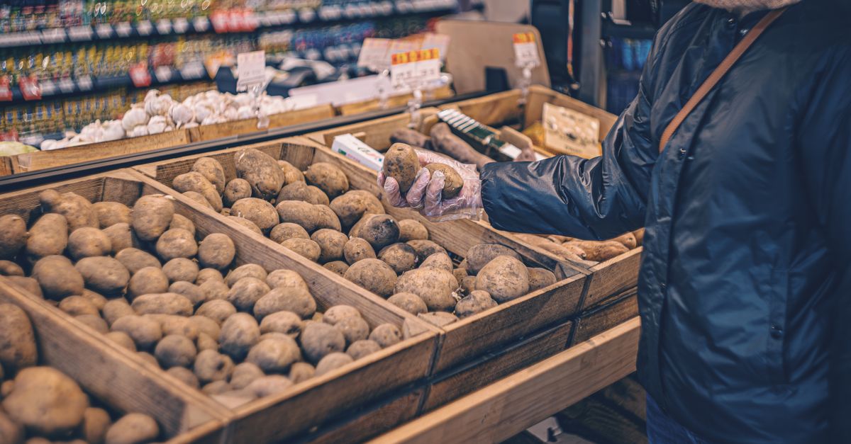Cassette di legno colme di patate esposte in un negozio, con una persona che le seleziona indossando un guanto