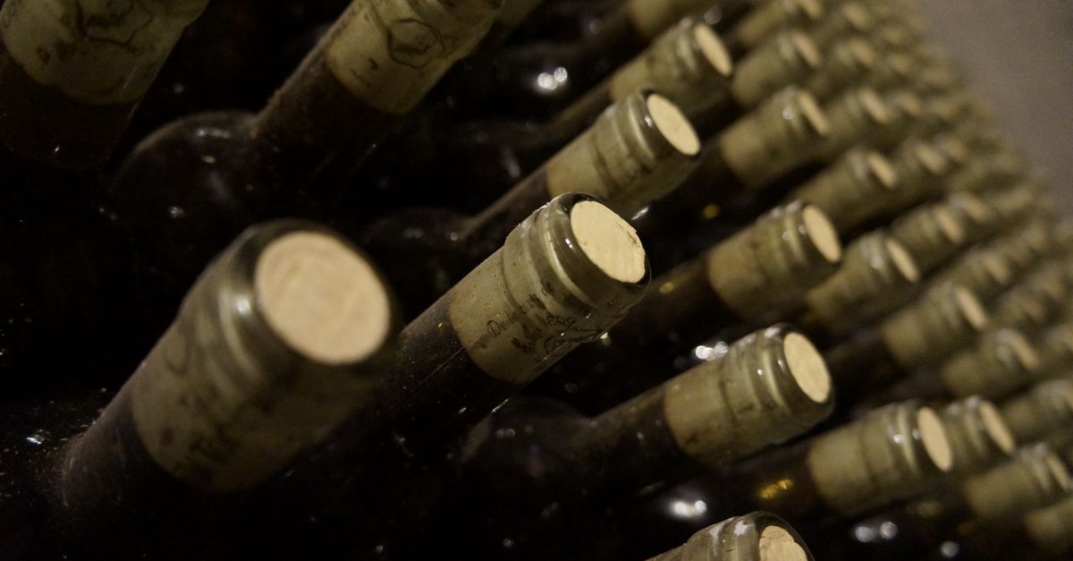 Bottiglie di vino sdraiate con tappi di sughero visibili, disposte in file su una cantina.