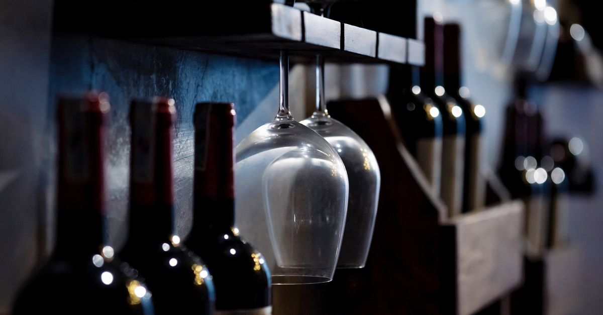 Bottiglie di vino scure allineate su una rastrelliera con bicchieri da vino appesi capovolti sopra di esse.
