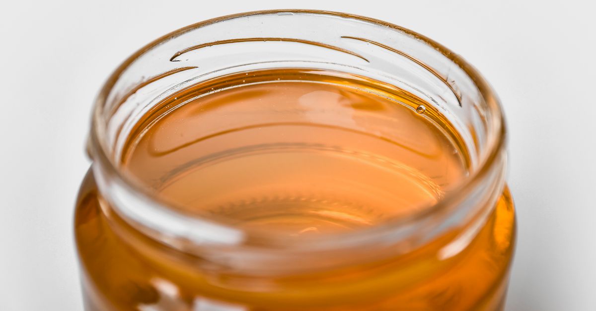 Primo piano di un barattolo di vetro aperto contenente miele liquido dorato e trasparente.