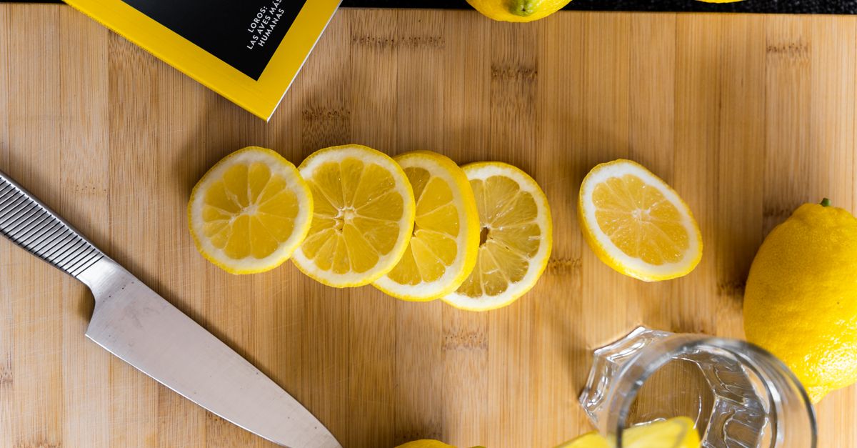 Un coltello da cucina su un tagliere di legno accanto a fette di limone appena tagliate