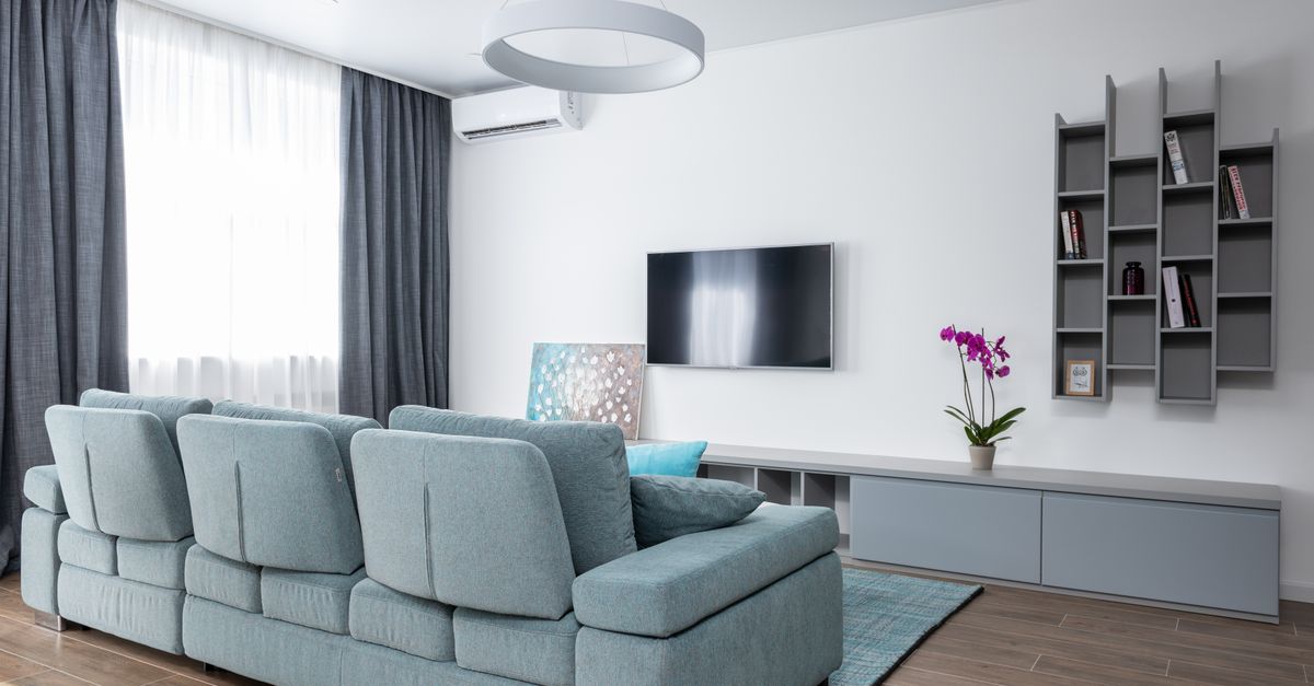 Soggiorno moderno con divano grigio-azzurro, mobile TV basso e libreria a mensole geometriche montata sulla parete accanto alla televisione.
